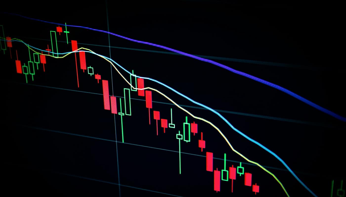 A stock market candlestick chart on a dark screen showing a falling trend