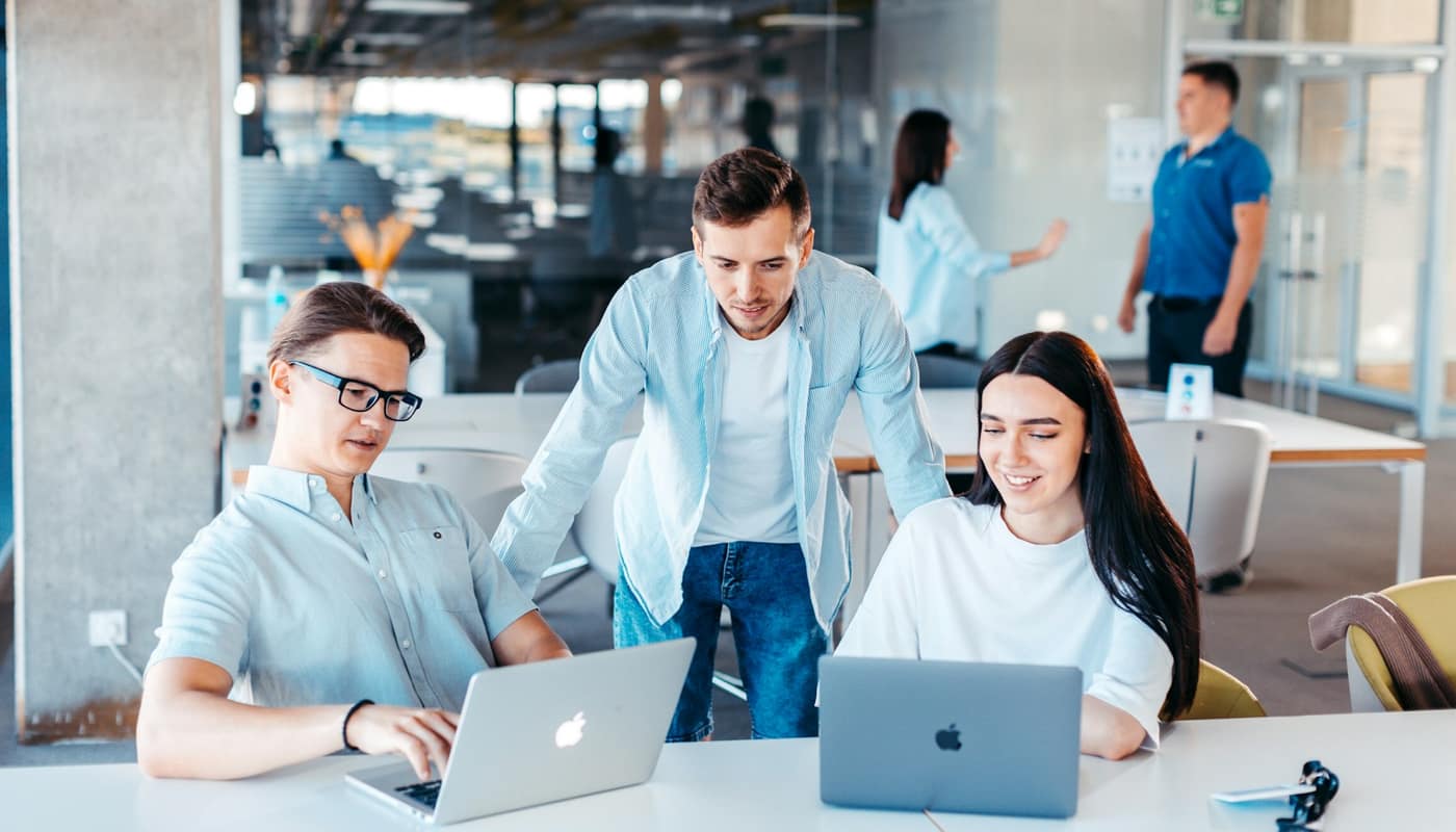 Three colleagues looking at laptops in a bright open-plan office